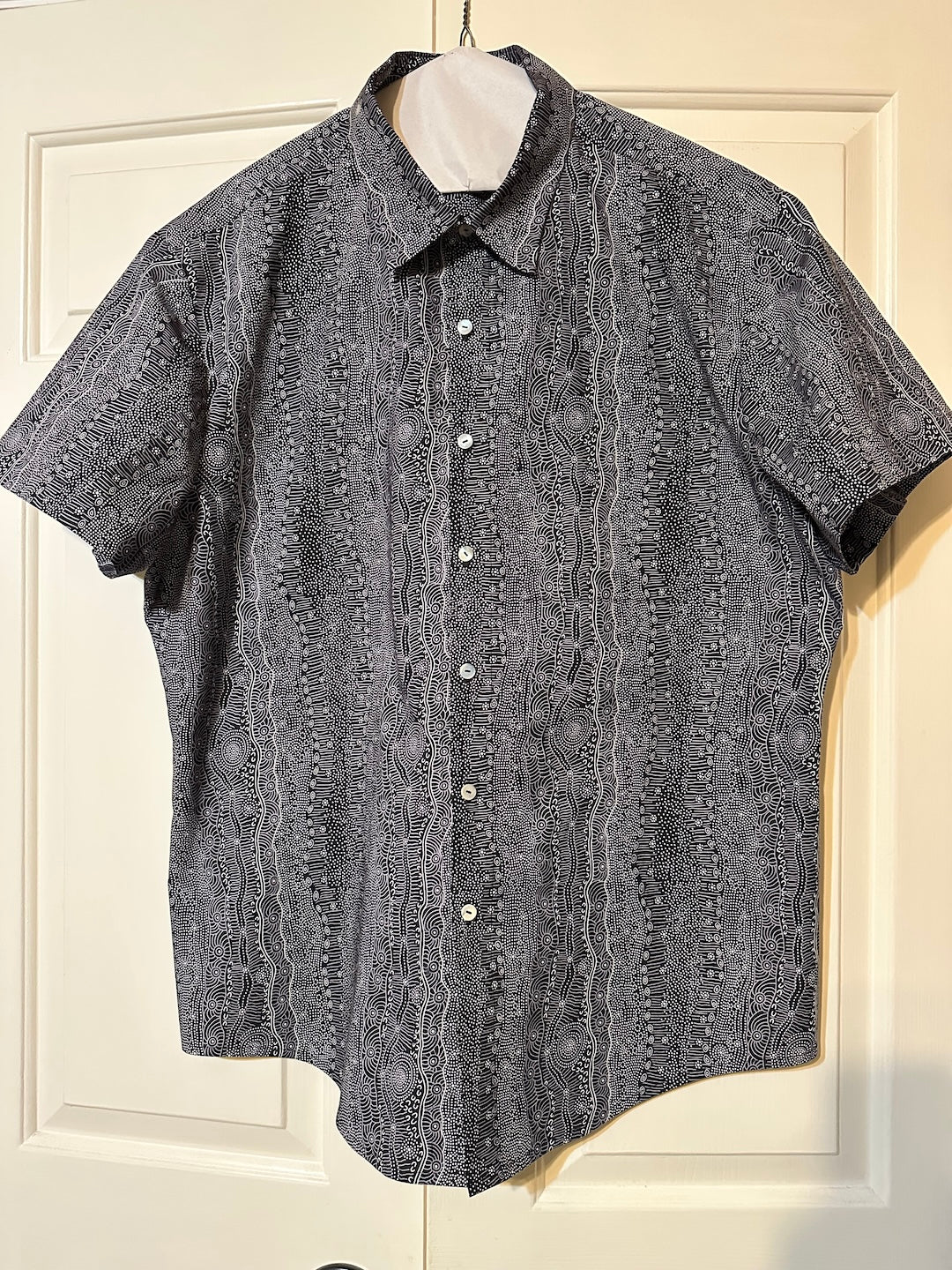 Short-sleeve hand made men's shirt with a pattern on a hanger against a white door background