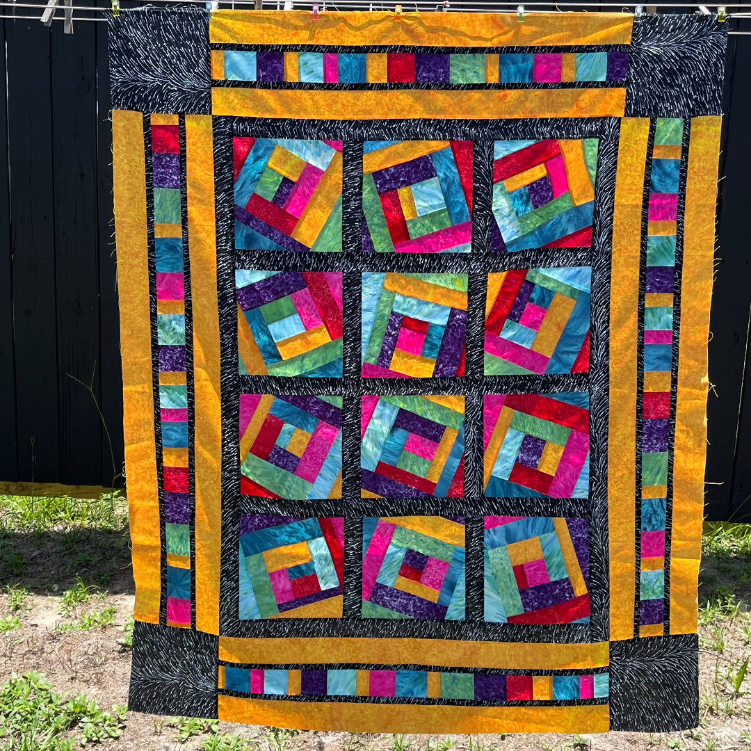 A colorful Log Cabin variation quilt in front of a fence