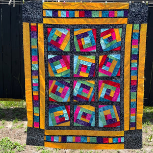 A colorful Log Cabin variation quilt in front of a fence