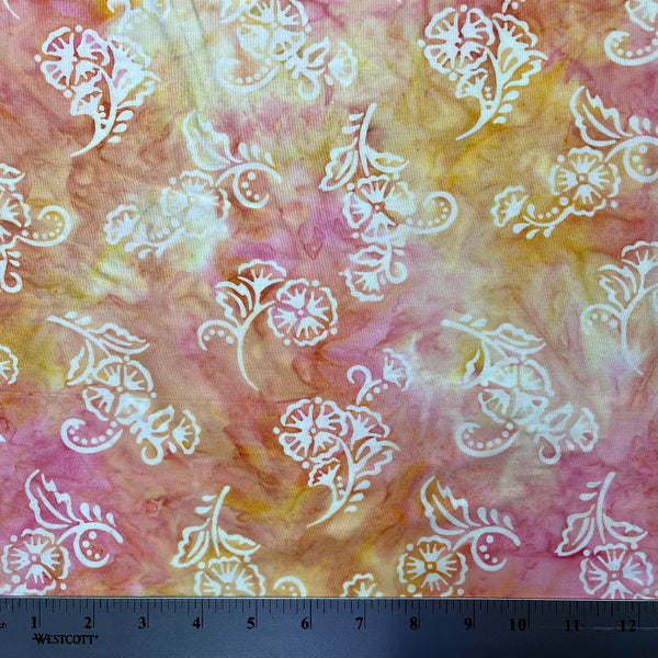 Fabric with white floral patterns on a tie-dye background, featuring pink and yellow colors.