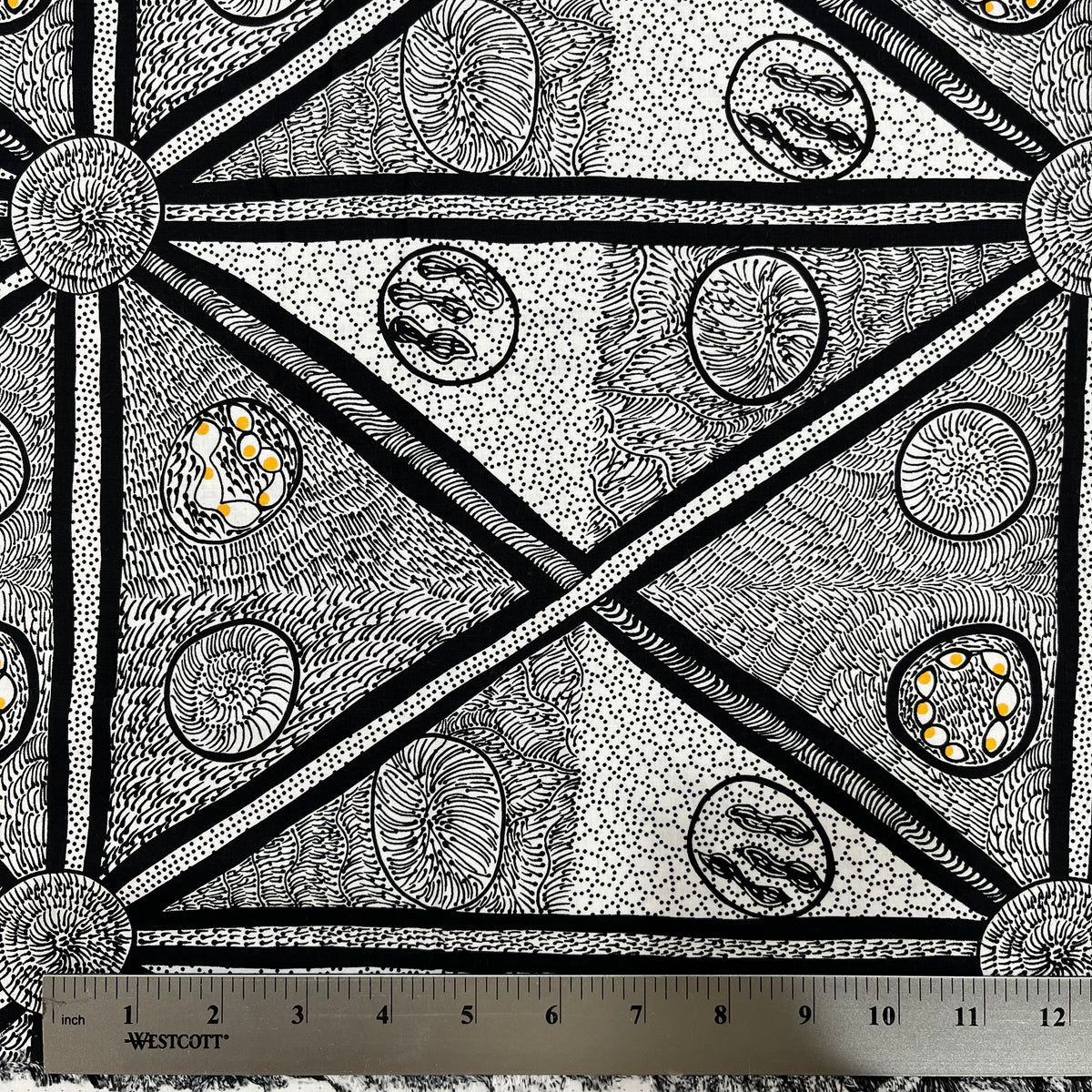 White and black fabric with abstract design, with a smidge of yellow, detail picture with ruler for scale