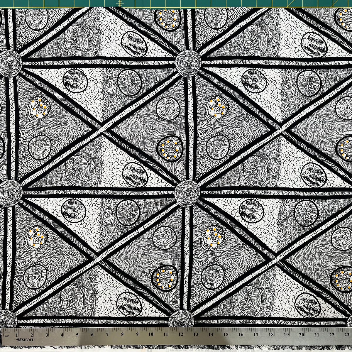 White and black fabric with abstract design, including a smidge of yellow, detail picture with ruler for scale