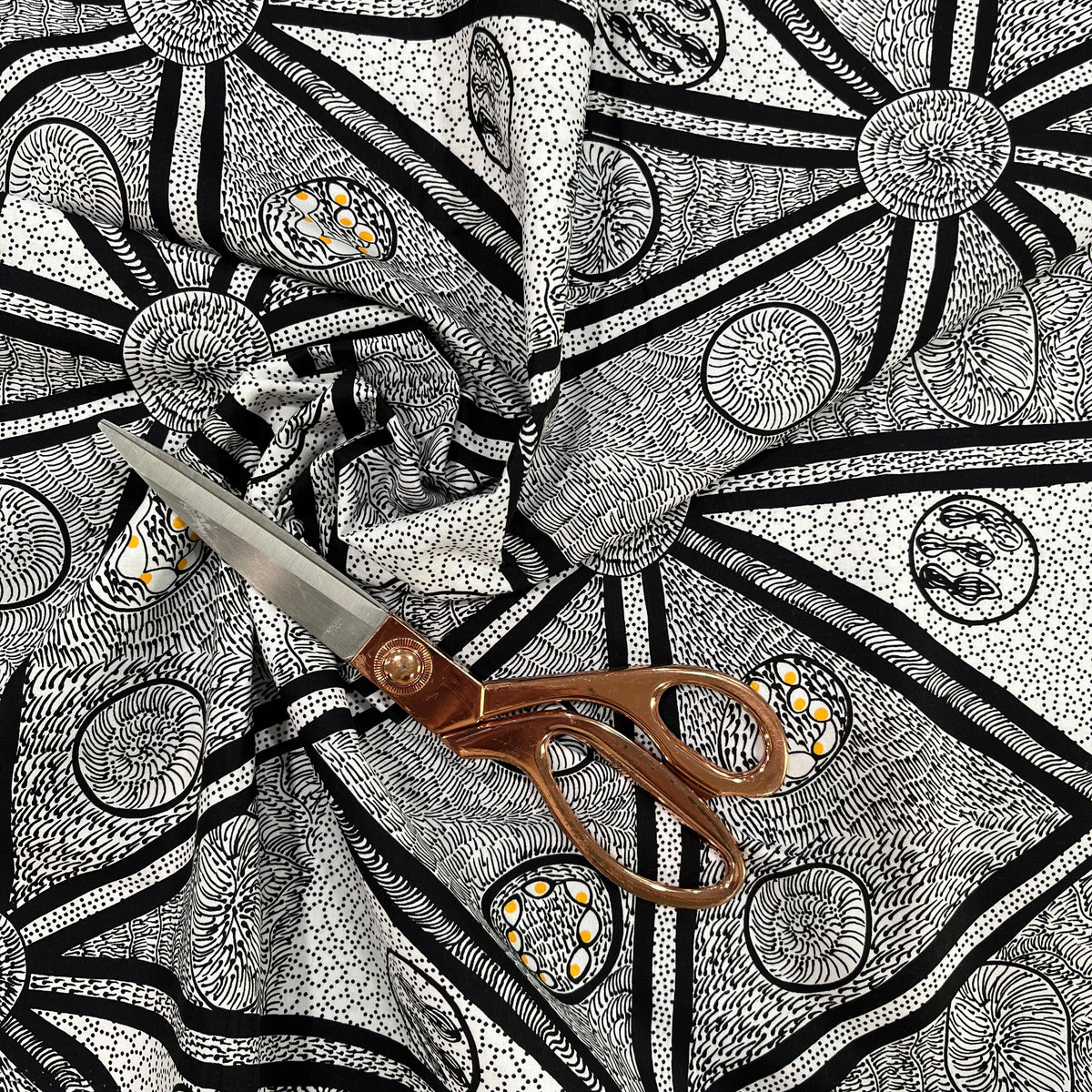 white, black and a tiny bit of yellow fabric with abstract design, shown in a decorative swirl with a pair of scissors on top