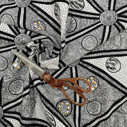 white, black and a tiny bit of yellow fabric with abstract design, shown in a decorative swirl with a pair of scissors on top