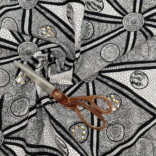 white, black and a tiny bit of yellow fabric with abstract design, shown in a decorative swirl with a pair of scissors on top