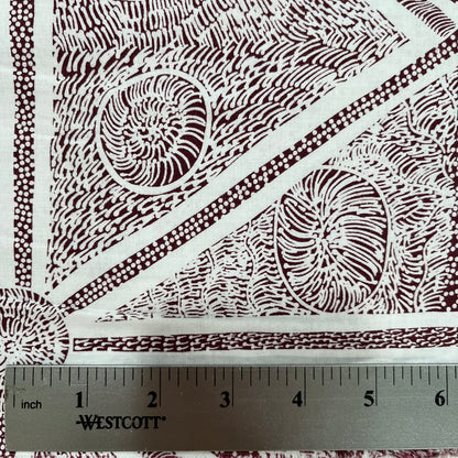 A close-up of a white fabric with a dark brown geometric and organic pattern, featuring a metal ruler at the bottom showing measurements in inches. 