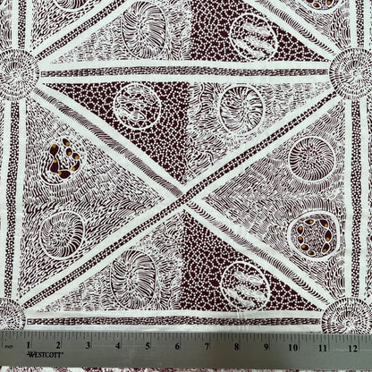 white and burgundy patterned fabric with a geometric design featuring triangles, dots, and lines, shown with a metal ruler at the bottom indicating scale.