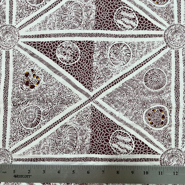 white and burgundy patterned fabric with a geometric design featuring triangles, dots, and lines, shown with a metal ruler at the bottom indicating scale.