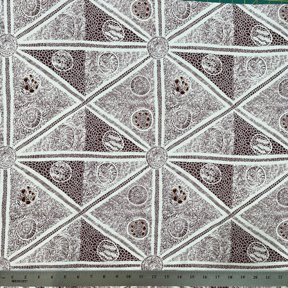 white and burgundy fabric with a repeating geometric pattern of triangles and circular medallions, shown with a metal ruler at the bottom indicating scale.