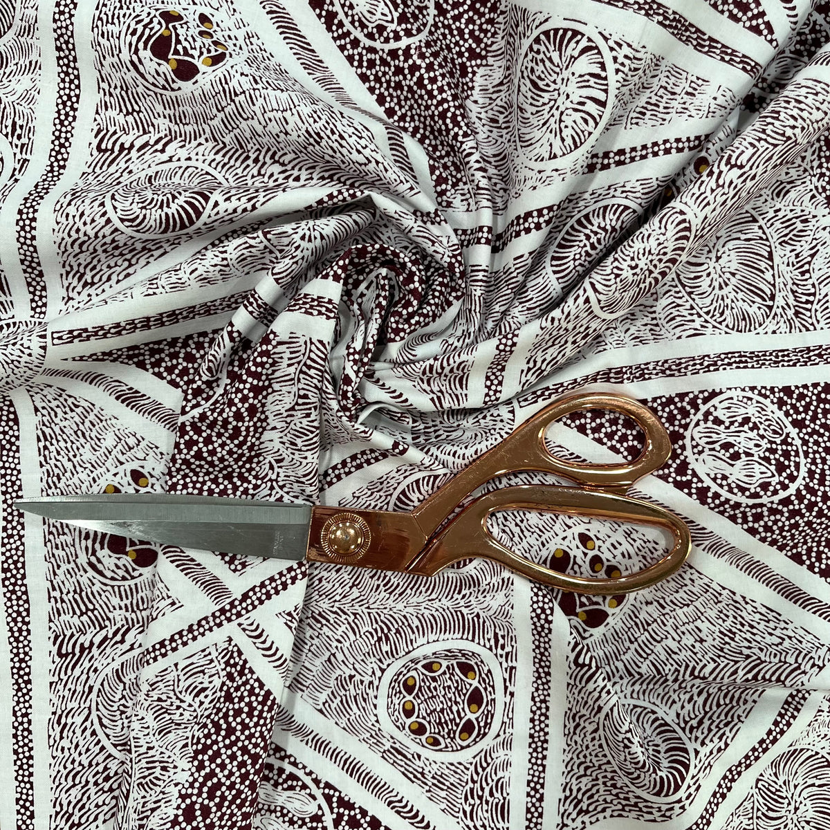 A close-up of patterned fabric with a brown and white abstract print, styled with a pair of bronze-colored scissors on top.
