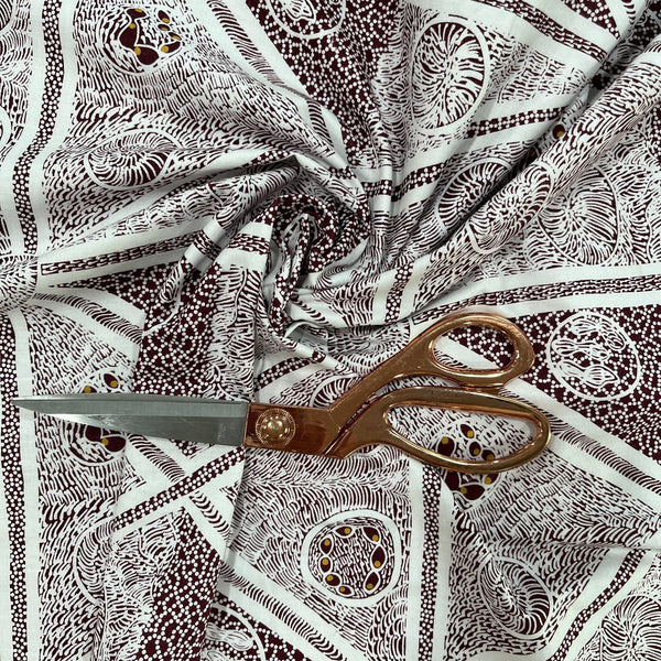 A close-up of patterned fabric with a brown and white abstract print, styled with a pair of bronze-colored scissors on top.