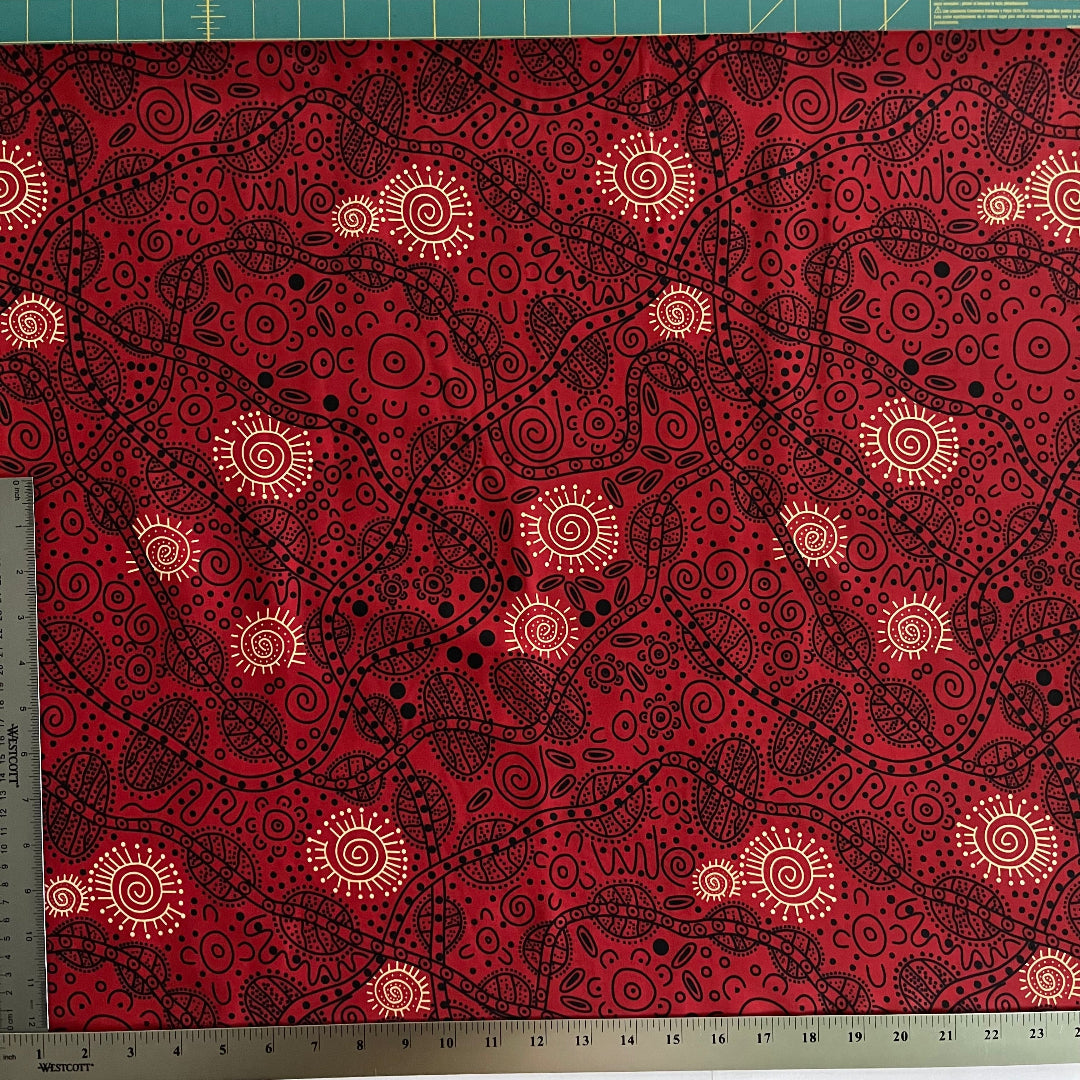 Red fabric with a black and yellow Aboriginal-style dot art pattern, shown with a metal ruler on the left side to indicate scale.