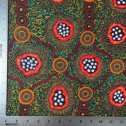 A close-up of patterned fabric with a ruler along the top and left edges for scale. The fabric has a black background covered in dense yellow and green leaf-like dots, with three large circular floral or abstract medallion motifs in red, orange, and light blue.