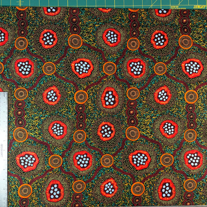 A close-up of patterned fabric with a ruler along the top and left edges for scale. The fabric has a black background covered in dense yellow and green leaf-like dots, with three large circular floral or abstract medallion motifs in red, orange, and light blue.