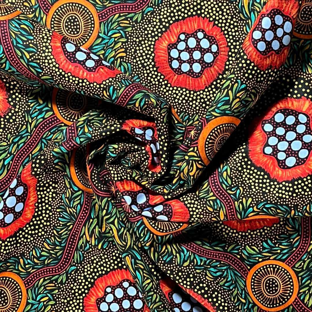 A close-up of patterned fabric with a bold abstract print featuring red, orange, light blue, teal, black, and beige dotted motifs arranged in a swirling, draped layout.