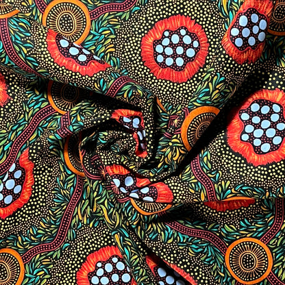 A close-up of patterned fabric with a bold abstract print featuring red, orange, light blue, teal, black, and beige dotted motifs arranged in a swirling, draped layout.