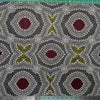 In this fabric, softly contrasting shades of grey, olive, burgundy, and white form patterns representing wind-scattered seeds and spinifex grasses—elements deeply rooted in desert life and culture.