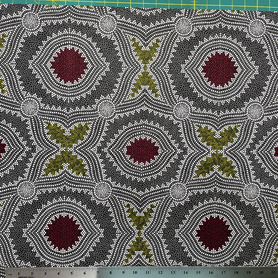 In this fabric, softly contrasting shades of grey, olive, burgundy, and white form patterns representing wind-scattered seeds and spinifex grasses—elements deeply rooted in desert life and culture.