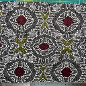 In this fabric, softly contrasting shades of grey, olive, burgundy, and white form patterns representing wind-scattered seeds and spinifex grasses—elements deeply rooted in desert life and culture.