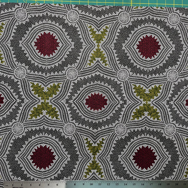 In this fabric, softly contrasting shades of grey, olive, burgundy, and white form patterns representing wind-scattered seeds and spinifex grasses—elements deeply rooted in desert life and culture.