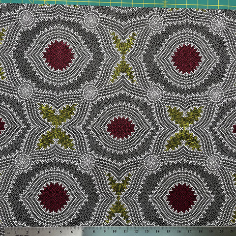 In this fabric, softly contrasting shades of grey, olive, burgundy, and white form patterns representing wind-scattered seeds and spinifex grasses—elements deeply rooted in desert life and culture.