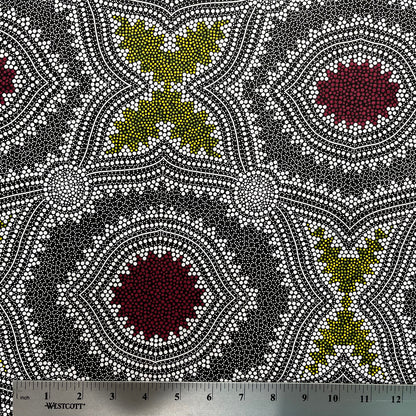 In this fabric, softly contrasting shades of grey, olive, burgundy, and white form patterns representing wind-scattered seeds and spinifex grasses—elements deeply rooted in desert life and culture.