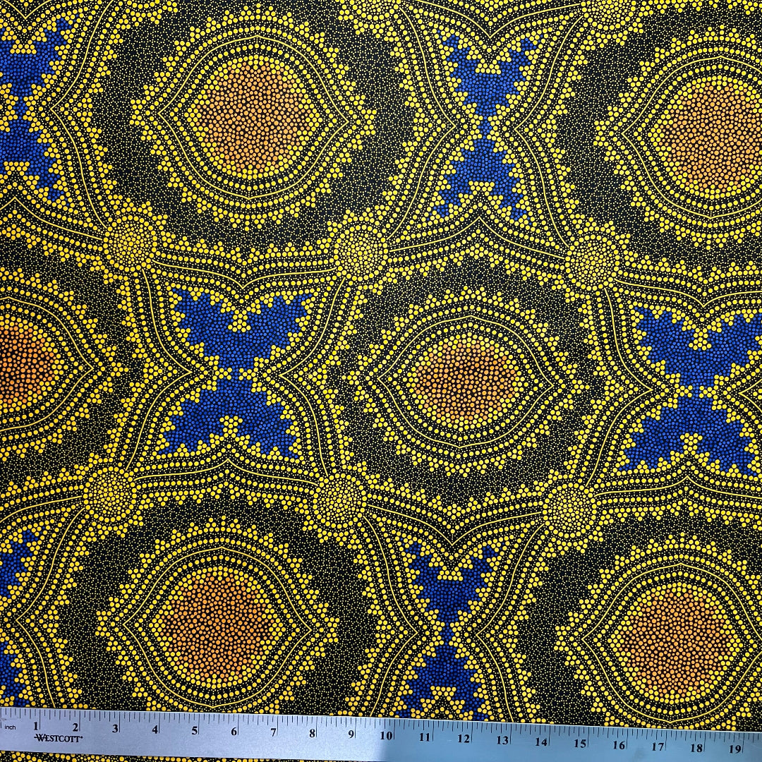 In this fabric, softly contrasting shades of gold, dark grey, blue and orange form patterns representing wind-scattered seeds and spinifex grasses—elements deeply rooted in desert life and culture.