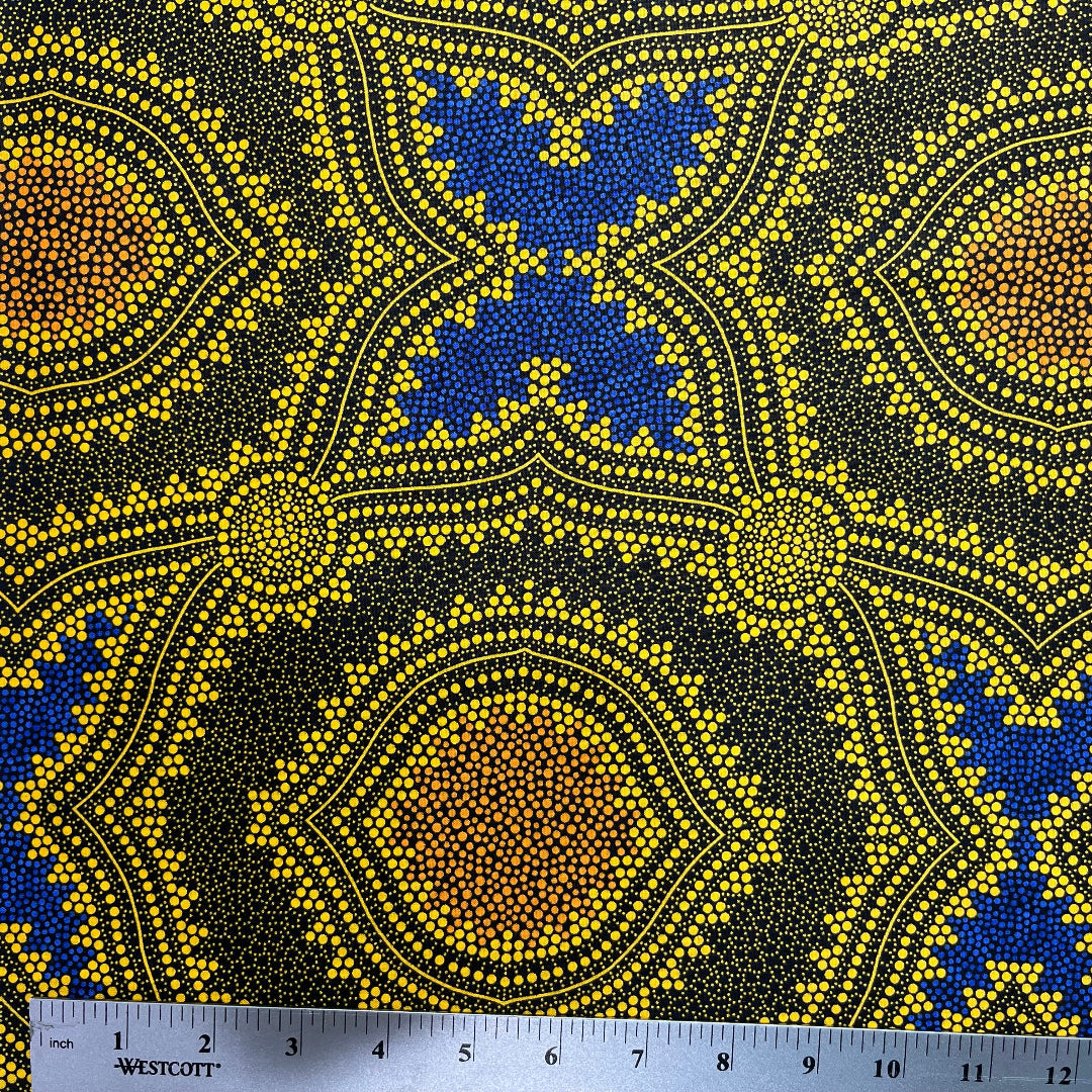 In this fabric, softly contrasting shades of gold, dark grey, blue and orange form patterns representing wind-scattered seeds and spinifex grasses—elements deeply rooted in desert life and culture.
