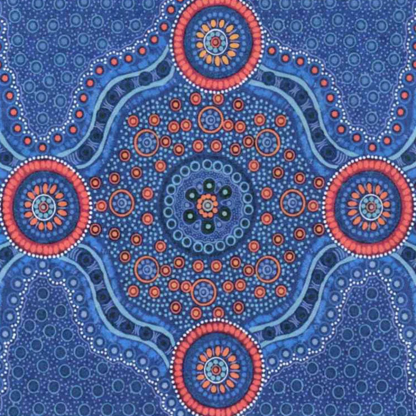A close-up of a blue patterned fabric  featuring a central circular mandala design with coral, blue and yellow dots on a blue background