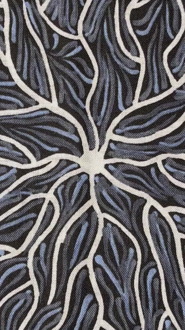 Running Water Dreaming grey is an intricate design of fine lines in white, grey and purplish grey on a black background, simulating the rivulets of water splashing from a central waterhole.